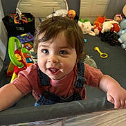 Noah joined the competition — help win amazing prizes! toddler, child, playpen, toys, stuffed_animals, indoor, curly_hair, blue_eyes, clothing, overalls, pink_shirt, smiling, happy, face, hand, baby_toy, play_area, colorful, person, young_child