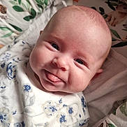 Winnie joined the competition — help win amazing prizes! baby, infant, face, tongue_out, smile, blue_eyes, floral_clothing, cute, child, cushion, leaf_pattern, soft_fabric, comfort, indoors, portrait, skin, head, lying_down, playful, happy