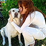 woman, dog, cat, pet, kiss, cuddle, outdoor, garden, greenery, portrait, white_dog, large_dog, feline, animal, person, sitting, kneeling, sunlight, grass, foliage