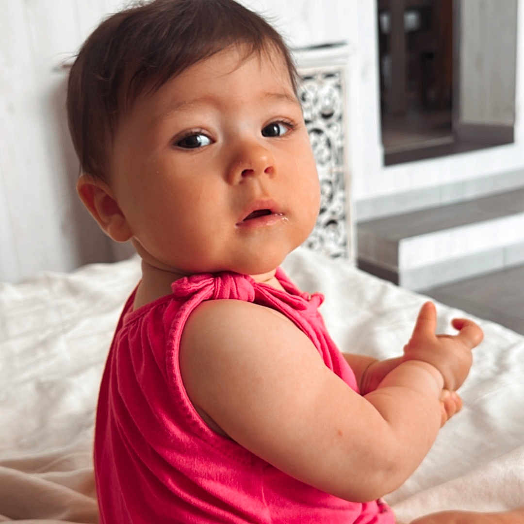 Nina participe au concours pour gagner de l'argent avec cette photo : baby, blanket, child, curious, cute, expression, face, floor, home, indoors, infant, person, pink_clothing, portrait, room, short_hair, sitting, skin, soft_light, young
