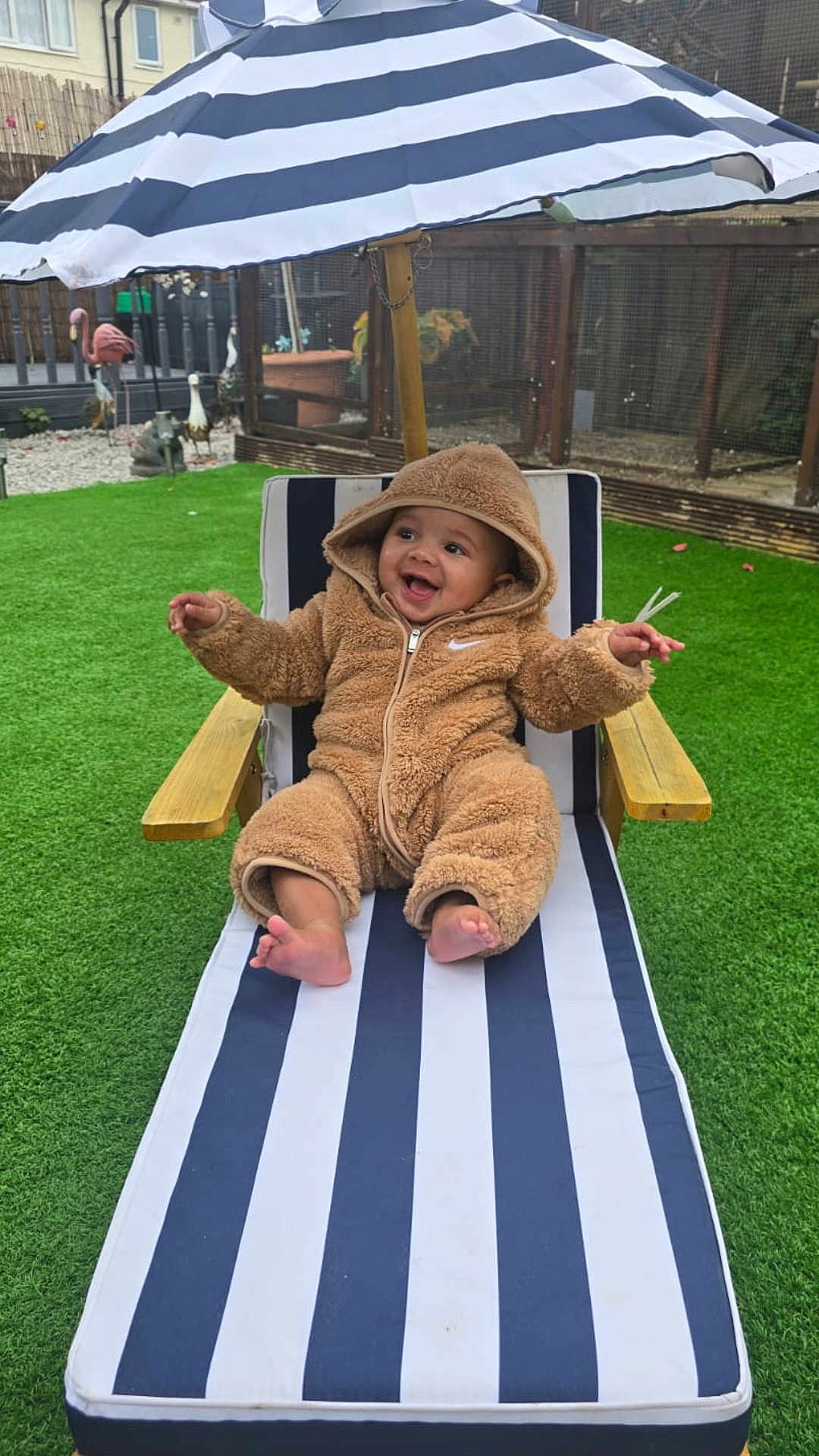 Ziggy joined the competition — help win amazing prizes! baby, child, smile, outdoor, lounge_chair, umbrella, striped, green_grass, happy, cozy_clothing, onesie, fence, garden, toes, wooden_armrest, cute, infant, playful, relaxing, hooded