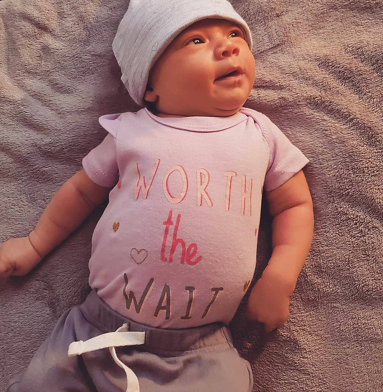 Emerie is registered to the contest to win money with this photo: arm, baby_toddler_clothing, cap, cheek, cool, face, facial_expression, finger, gesture, hand, happy, headwear, human_body, lip, neck, nose, person, pink, skin, sleeve