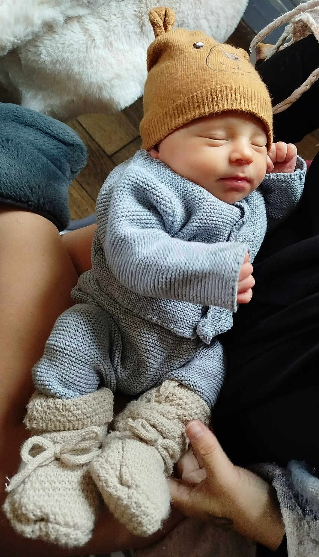 Gaston participe au concours pour gagner de l'argent avec cette photo : baby, newborn, sleeping, knitted_clothing, hat, bear_ears, boots, hands, person, cozy, warm, indoor, wood_floor, blanket, soft_texture, cuddly, infant, cute, resting, portrait
