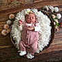 baby, newborn, sleeping, pink_overalls, white_booties, fluffy_blanket, basket, flowers, wooden_floor, peaceful, infant, headband, soft_lighting, portrait, cozy, cute, resting, indoor, child, adorable