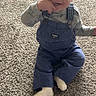 Carter is registered to the contest to win money with this photo: baby, child, smiling, sitting, carpet, indoor, overalls, clothing, person, cute, happy, toddler, floor, playful, finger_in_mouth, head, face, sock, infant, light