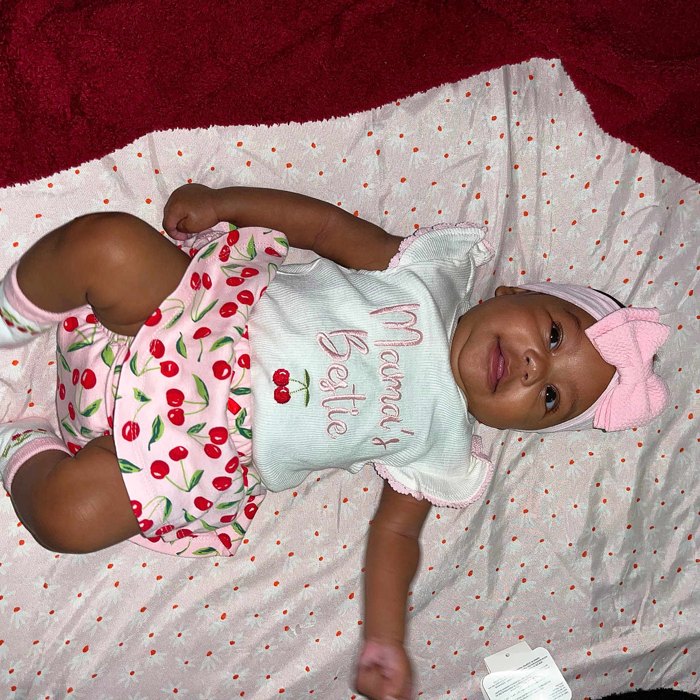 Makenzee is registered to the contest to win money with this photo: baby, blanket, cherry_pattern, child, clothing, cute, happy, headband, indoor, infant, laying_down, pink, polka_dot, portrait, red_blanket, skirt, smiling, soft_texture, toddler, white_top