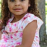 child, girl, curly_hair, hair_bows, pink_dress, floral_pattern, outdoor, nature, tree, smile, portrait, young_child, sunlight, park, cute, happy, face, summer, greenery, casual_clothing