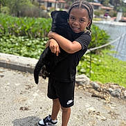 Ak joined the competition — help win amazing prizes! child, puppy, black_dog, outdoor, smiling, braids, nike, shorts, sneakers, water, greenery, daylight, happy, person, nature, pet, holding, portrait, casual_clothing, playful