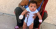 Azure is registered to the contest to win money with this photo: baby, woman, tattoos, red_braids, socks, crocs, outdoor, concrete, wall, smiling, holding, person, child, footwear, casual, bracelet, earrings, pacifier_clip, curly_hair, crouching