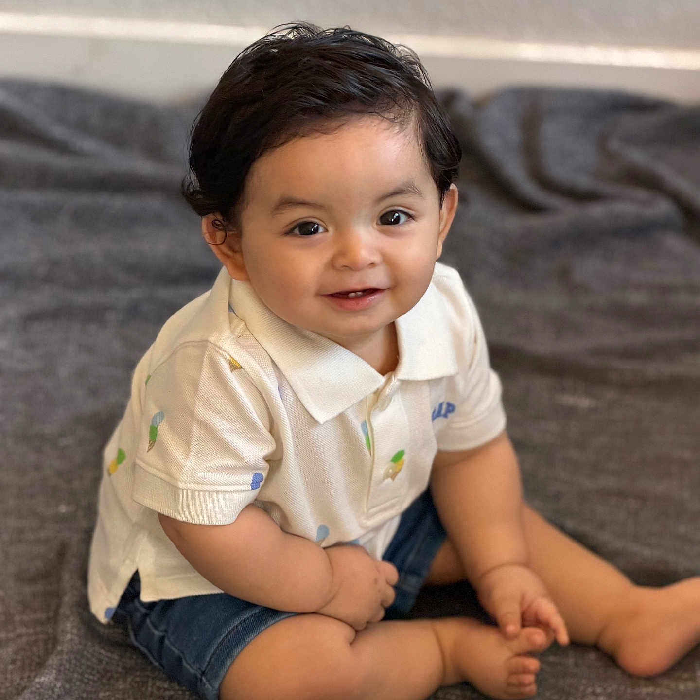 Mateo Magana joined the competition — help win amazing prizes! baby, child, toddler, smiling, sitting, polo_shirt, denim_shorts, indoor, blanket, cute, happy, face, hair, eyes, skin, person, clothing, foot, hand, portrait