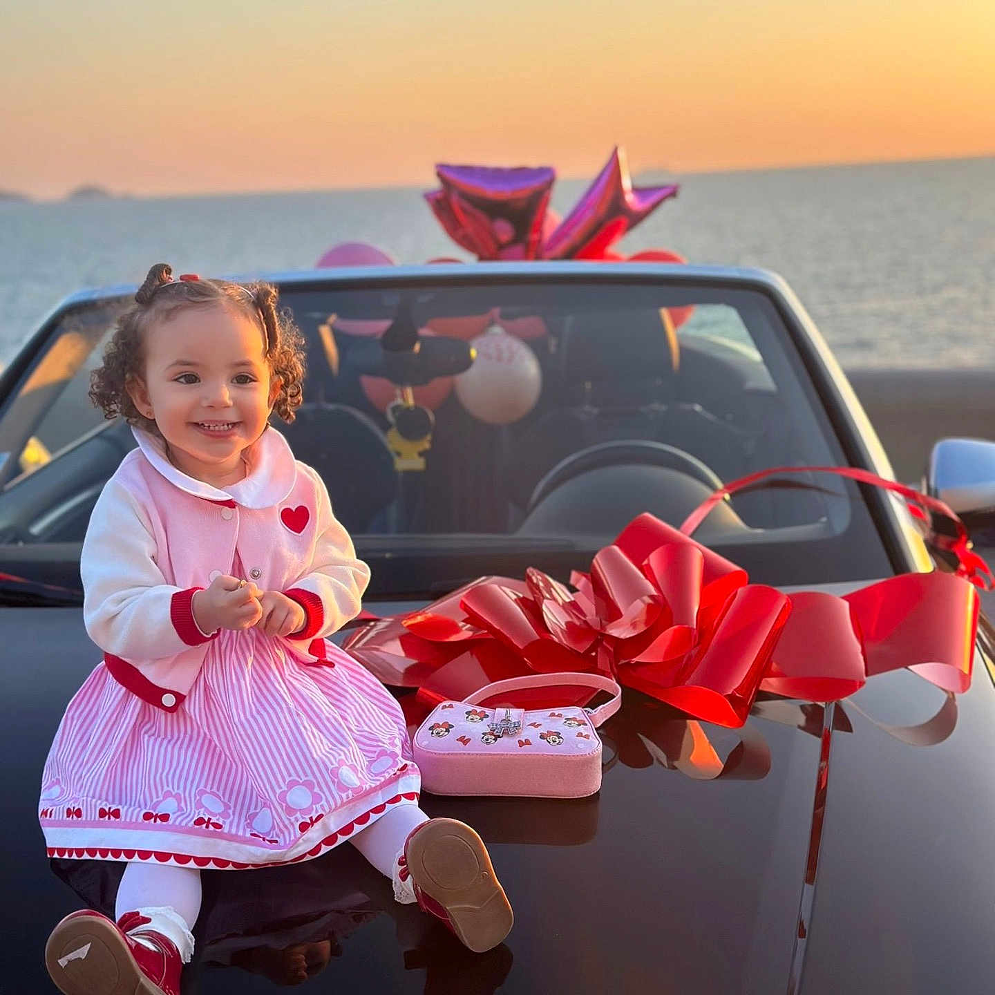 Ayline participe au concours pour gagner de l'argent avec cette photo : child, toddler, car, red_bow, sunset, ocean, pink_dress, smiling, curly_hair, outdoor, happy, toy_purse, balloons, reflection, vehicle, holiday, celebration, cute, fashion, portrait