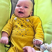 Louis participe au concours pour gagner de l'argent avec cette photo : baby, smiling, yellow_clothing, onesie, infant, cushion, plush_toy, hand, happy, face, person, indoors, child, cute, soft_toy, playful, skin, newborn, lying_down, holding