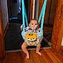 baby, child, indoor, jumper, pacifier, wooden_floor, doorway, blue_straps, colorful, toy, infant, person, face, legs, barefoot, home, playing, hanging, cute, curious