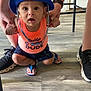 Keanu is registered to the contest to win money with this photo: child, toddler, hat, blue_hat, orange_shirt, daddy_s_dude_shirt, shorts, flip_flops, indoor, wooden_floor, person_holding_child, hands, squatting, expression_surprised, footwear, adult_legs, black_shoes, flooring, casual_clothing, child_fashion