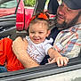 toddler, child, man, car, window, seat, smile, hair_bow, orange_clothing, cap, beard, plaid_shirt, hand, red_truck, outdoor, greenery, happy, family, portrait, casual