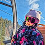 Enola a rejoint le concours — aidez-le/la à gagner de superbes lots ! child, ski_goggles, winter_clothing, hat, playful_hat, gondola, cabin, mountain, forest, sky, winter, snow, outdoor, reflection, colorful_jacket, pink, blue, seat, scenery, sunlight