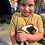 Mateo is registered to the contest to win money with this photo: child, smiling, guinea_pig, pet, indoor, casual_clothing, curly_hair, animal, holding, happy, person, floor, furniture, crutches, background, soft_lighting, domestic, cute, portrait, home