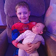 Roman-Paul joined the competition — help win amazing prizes! child, baby, spiderman_costume, armchair, smiling, holding, indoor, family, cute, infant, pajamas, sibling, happy, portrait, cozy, furniture, relaxed, toddler, person, home