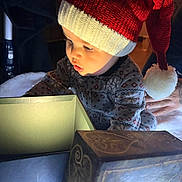 Xavian is registered to the contest to win money with this photo: toddler, child, hat, knit_hat, red_hat, holiday, christmas, box, light, curious, indoor, person, baby, patterned_clothing, pom_pom, hand, warm_lighting, exploring, cozy, festive