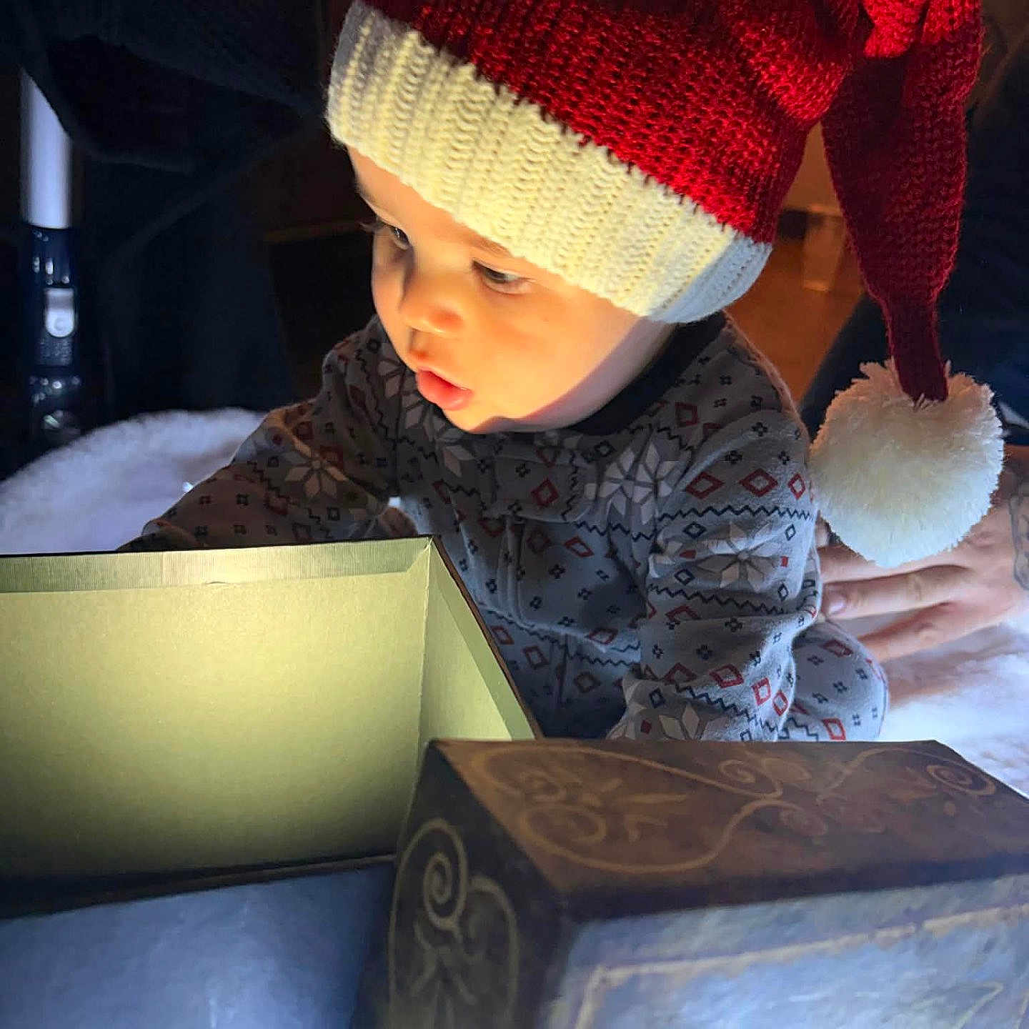 Xavian is registered to the contest to win money with this photo: baby, box, child, christmas, cozy, curious, exploring, festive, hand, hat, holiday, indoor, knit_hat, light, patterned_clothing, person, pom_pom, red_hat, toddler, warm_lighting