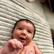 Xavian is registered to the contest to win money with this photo: baby, blanket, close_up, cute, expression, face, hand, happy, indoors, infant, joyful, lying_down, newborn, person, skin, smiling, soft_light, supporting_hand, tender, texture
