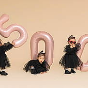 Olivia is registered to the contest to win money with this photo: toddler, child, balloon, number_balloon, black_dress, boots, red_sunglasses, heart_shaped_sunglasses, posing, studio, beige_background, celebration, party, cute, fashion, playful, indoor, three_children, smiling, fun