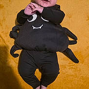 Elsie joined the competition — help win amazing prizes! baby, child, smiling, costume, spider, black_clothing, infant, lying_down, yellow_background, cute, happy, hands, feet, indoors, carpet, portrait, face, expressive, funny, playful