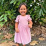 child, girl, smiling, pink_dress, outdoor, greenery, leaves, sandals, happy, young_child, nature, portrait, standing, sunlight, bracelet, short_hair, face, cute, fashion, daylight