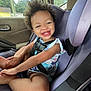 toddler, child, car_seat, smiling, curly_hair, happy, inside_car, seatbelt, casual_clothing, playful, young_child, daylight, window, car_door, skin, person, portrait, cute, legs, hands