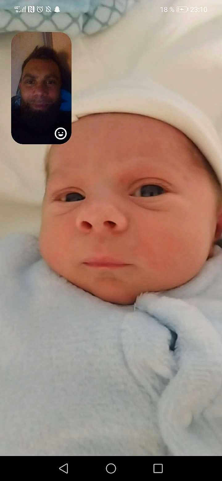 Nolann participe au concours pour gagner de l'argent avec cette photo : baby, infant, close_up, blanket, blue_clothing, face, headwear, newborn, swaddled, portrait, video_call, inset, man, beard, expression, indoor, technology, communication, screen, soft_texture