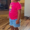 child, curly_hair, denim_shorts, earring, fashion, fireplace, flooring, full_body, home, indoor, necklace, photography, pink_shirt, portrait, serious_expression, sneakers, standing, toddler, wood_paneling, wooden_floor