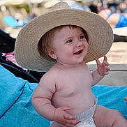 Maria a rejoint le concours — aidez-le/la à gagner de superbes lots ! baby, child, hat, straw_hat, diaper, smiling, happy, blue_towel, outdoor, beach, sunny, skin, face, hand, sitting, cute, summer, people, blurred_background, infant