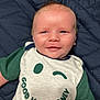 Abel is registered to the contest to win money with this photo: baby, smiling, infant, tshirt, text, good_vibes_only, winking_smiley, green_sleeves, lying_down, blanket, quilted, cute, happy, face, skin, head, blue_eyes, clothing, child, person