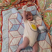 Abel joined the competition — help win amazing prizes! baby, infant, onesie, mittens, quilt, patterned_blanket, smiling_sun, text_on_clothing, raising_arm, lying_down, colorful, fabric, cute, happy, child, indoors, soft_texture, comfort, playful, portrait