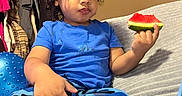 Roberto joined the competition — help win amazing prizes! blanket, blue_pants, blue_shirt, camouflage, casual_clothing, child, couch, curly_hair, expression, face, food, furniture, hand, indoor, relaxed, room, sitting, snack, toddler, watermelon