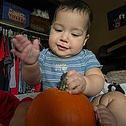 Roberto is registered to the contest to win money with this photo: baby, child, pumpkin, indoor, clothing, blue_shirt, hands, feet, face, smile, curious, furniture, bed, blanket, toy, cute, person, infant, skin, room