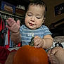 baby, child, pumpkin, indoor, clothing, blue_shirt, hands, feet, face, smile, curious, furniture, bed, blanket, toy, cute, person, infant, skin, room