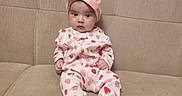 Osiyo is registered to the contest to win money with this photo: baby, beige, child, clothing, comfortable, couch, cute, headband, home, indoor, infant, looking_at_camera, onesie, person, pink_bow, portrait, seated, soft_fabric, strawberry_pattern, young_child