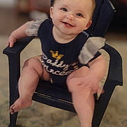 Charlotte Elishka is registered to the contest to win money with this photo: baby, child, smile, happy, sitting, chair, clothing, indoor, cute, person, infant, puffy_sleeves, navy_outfit, text_on_clothing, footwear_free, legs, face, head, furniture, carpet