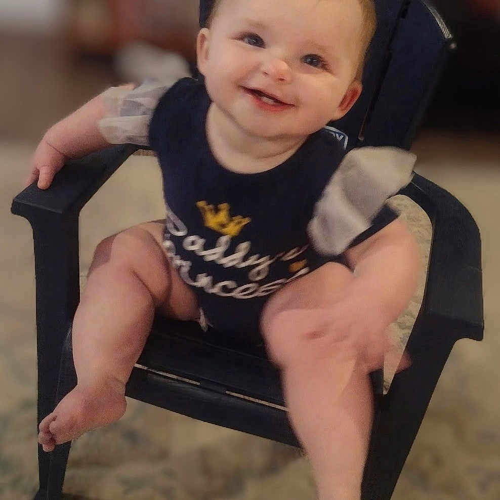Charlotte Elishka is registered to the contest to win money with this photo: baby, carpet, chair, child, clothing, cute, face, footwear_free, furniture, happy, head, indoor, infant, legs, navy_outfit, person, puffy_sleeves, sitting, smile, text_on_clothing
