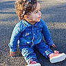 child, toddler, curly_hair, headband, denim_outfit, pink_shoes, sitting, asphalt, playground, sunny, outdoor, smiling, happy, casual_clothing, young_child, daylight, nature_background, fence, greenery, shadow