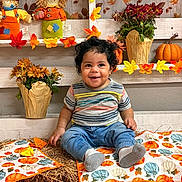 Josiah joined the competition — help win amazing prizes! baby, child, smiling, curly_hair, fall_decorations, pumpkin, scarecrow, flowers, hay_bale, autumn, seasonal, striped_shirt, blue_pants, socks, indoor, decor, orange, yellow, green, cute