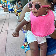 A Niylah joined the competition — help win amazing prizes! accessory, adult, baby, casual_clothing, child, colorful, curious, fun, holding, outdoor, people, person, pink_bib, playful, sidewalk, street, summer, sunglasses, sunny, umbrella