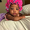 A Niylah is registered to the contest to win money with this photo: baby, infant, pink_bonnet, blanket, plush, soft_toys, bedroom, indoor, curious, cute, child, portrait, relaxing, cozy, sleepwear, face, headwear, skin, person, young_child