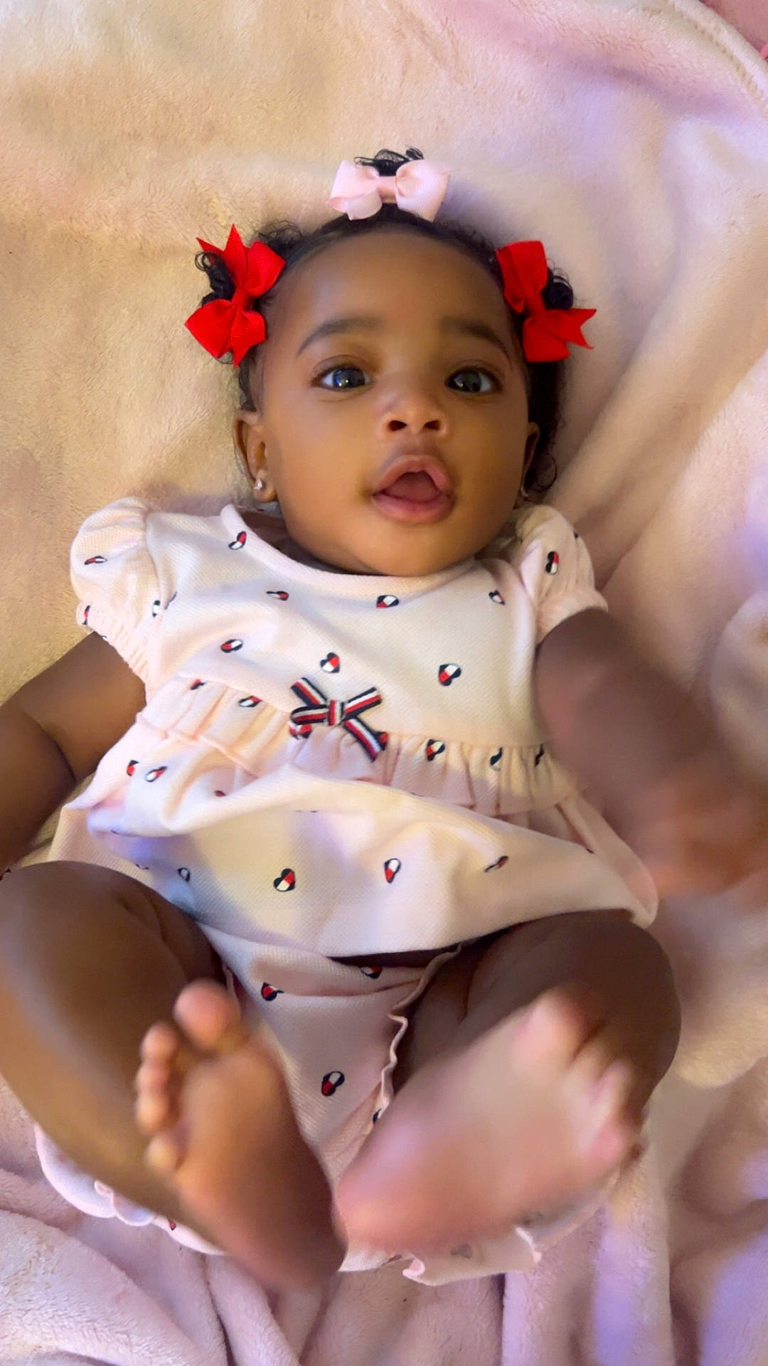 A Niylah is registered to the contest to win money with this photo: adorable, baby, blanket, bows, child, closeup, curious, cute, cute_expression, dress, feet, hair_bows, hands, indoor, infant, person, portrait, smiling, soft_texture, young_child