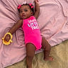 baby, infant, child, pink_onesie, hair_bows, yellow_toy, blanket, sand, outdoor, lying_down, cute, playful, skin, person, summer, beach, small_child, adorable, expression, relaxed