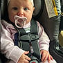 baby, child, car_seat, pacifier, headband, safety_harness, pink_clothing, hands, blue_eyes, infant, seatbelt, cute, portrait, indoor, closeup, child_safety, baby_girl, seat, straps, car_interior
