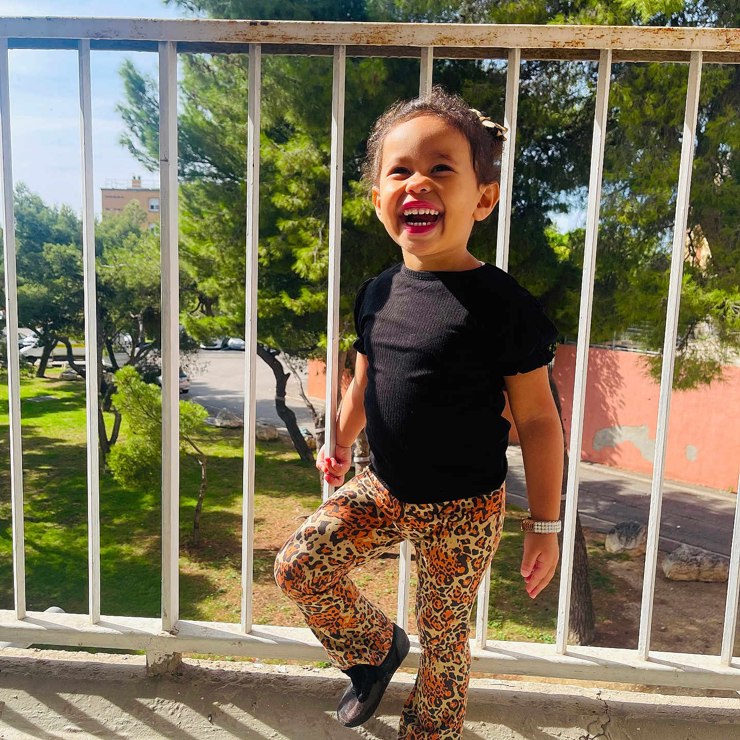 Melissa a rejoint le concours — aidez-le/la à gagner de superbes lots ! child, smiling, leopard_print, pants, black_shirt, balcony, railing, sunlight, shadow, trees, outdoor, happy, person, footwear, watch, daylight, nature, urban, playful, portrait