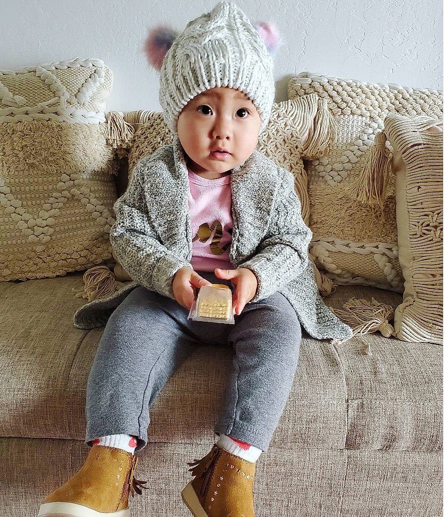 Infinity is registered to the contest to win money with this photo: beanie, beige, bonnet, cap, child, child_model, clothing, ear, hat, headgear, knit_cap, knitting, outerwear, person, sitting, sleeve, sweater, toddler, wool, woolen