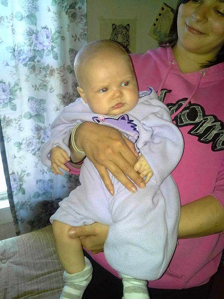 Kayleigh is registered to the contest to win money with this photo: baby, casual_clothing, child, cozy, curtains, face, floral_pattern, hand, holding, home, hoodie, indoor, infant, onesie, person, purple_clothing, smile, socks, tiger_drawing, woman